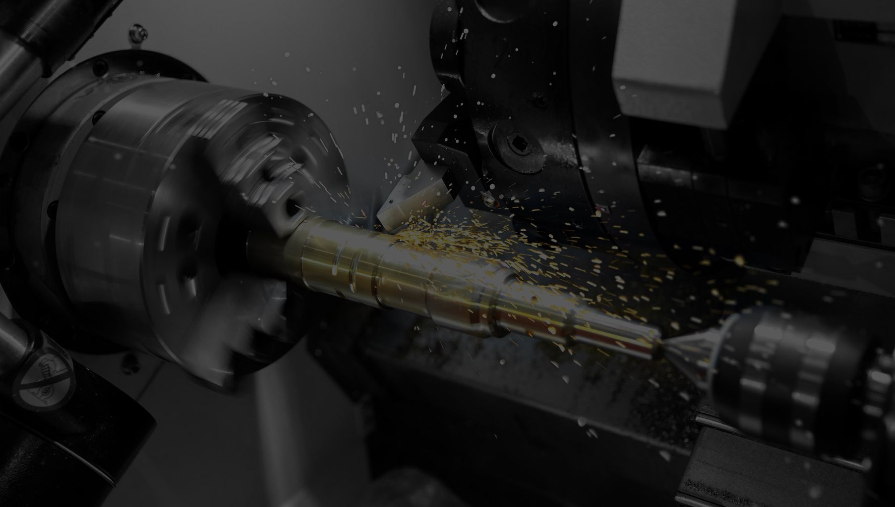 A metal rod is being machined on a lathe, sparks flying during grinding.